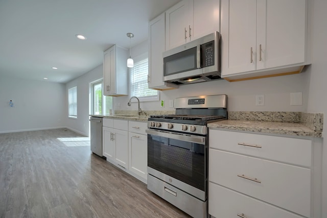 kitchen with sink, light hardwood / wood-style flooring, appliances with stainless steel finishes, white cabinetry, and hanging light fixtures