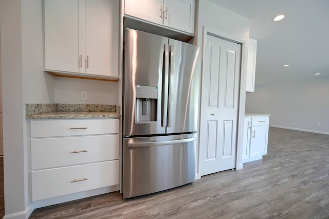 kitchen featuring stainless steel fridge, light stone countertops, and white cabinets