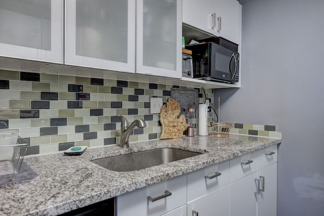 kitchen featuring light stone countertops, sink, white cabinets, and decorative backsplash