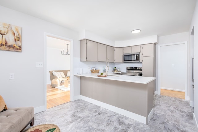 kitchen with appliances with stainless steel finishes, sink, gray cabinetry, a notable chandelier, and kitchen peninsula