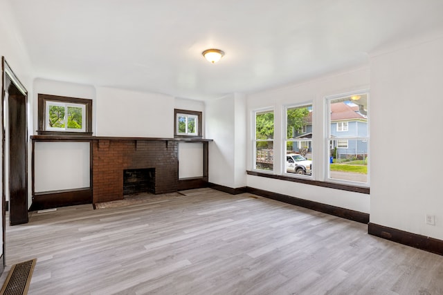 unfurnished living room featuring a brick fireplace, light hardwood / wood-style flooring, and a healthy amount of sunlight