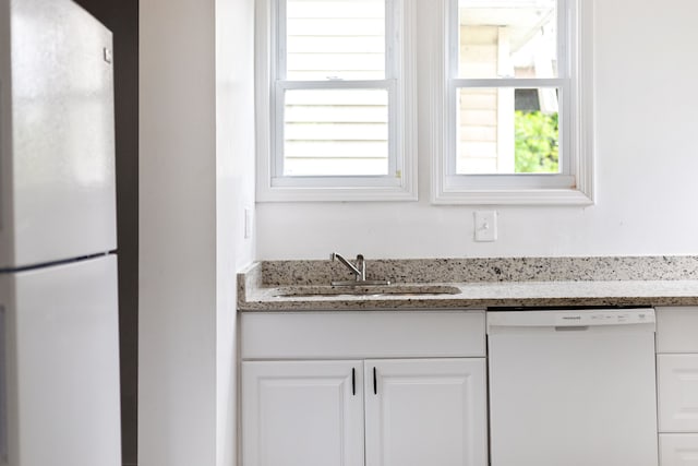 kitchen with light stone countertops, sink, white cabinets, and white appliances