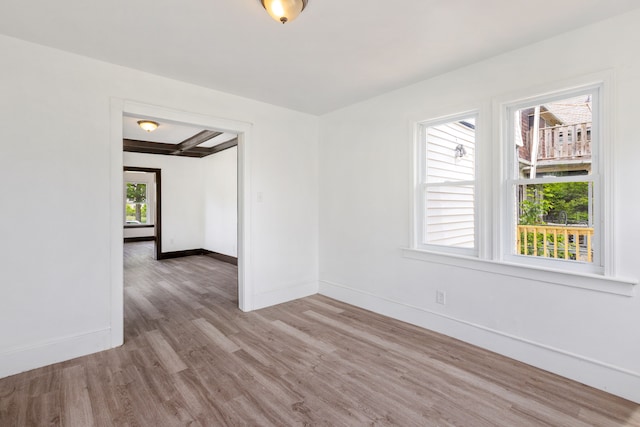 empty room featuring beam ceiling and light hardwood / wood-style floors