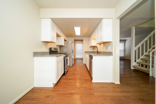 kitchen featuring sink, appliances with stainless steel finishes, white cabinetry, light stone countertops, and light wood-type flooring