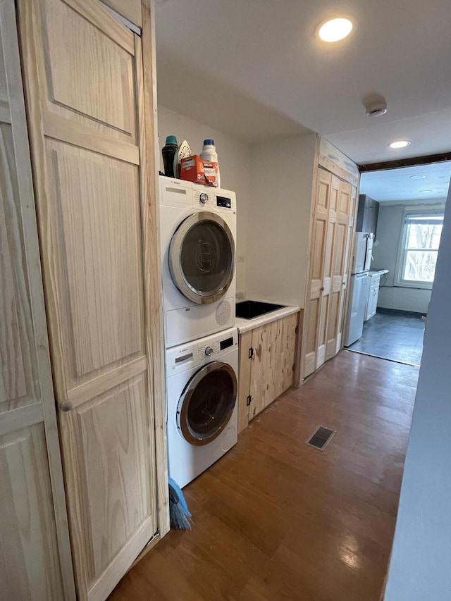 washroom featuring cabinets, stacked washer / drying machine, and dark hardwood / wood-style flooring