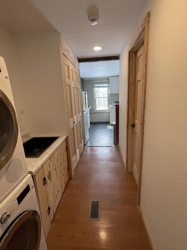 laundry room featuring cabinets, stacked washer and dryer, and light wood-type flooring