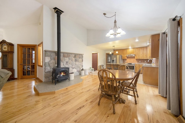 dining room featuring sink, a chandelier, high vaulted ceiling, light hardwood / wood-style flooring, and a wood stove