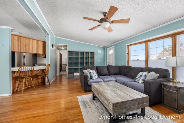 living room with lofted ceiling, light wood-type flooring, ceiling fan, crown molding, and a textured ceiling