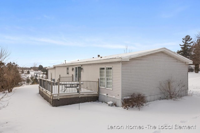 snow covered back of property with a wooden deck