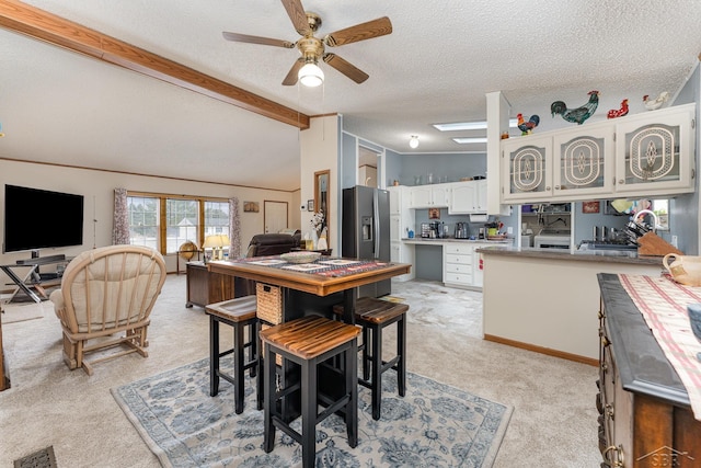 carpeted dining space with ceiling fan, vaulted ceiling with beams, and a textured ceiling