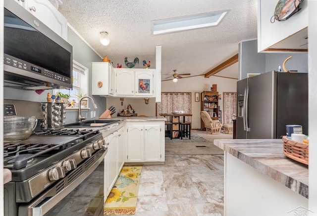 kitchen with sink, appliances with stainless steel finishes, lofted ceiling with beams, a textured ceiling, and white cabinets