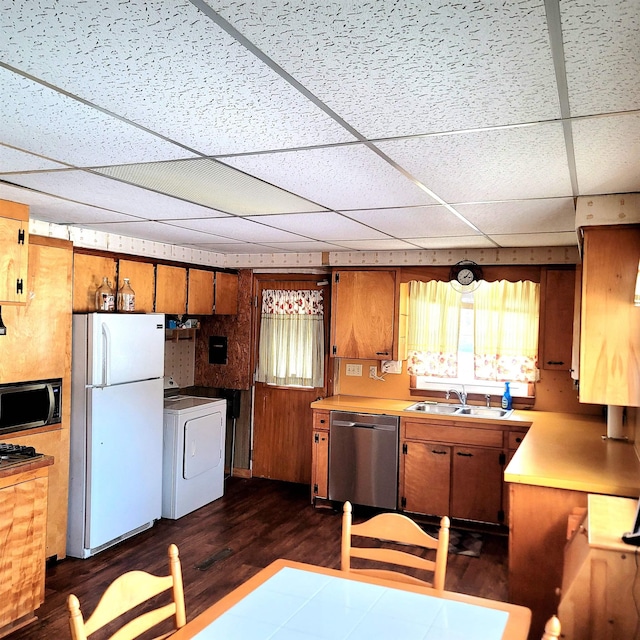 kitchen with appliances with stainless steel finishes, dark hardwood / wood-style floors, a paneled ceiling, washer / clothes dryer, and sink