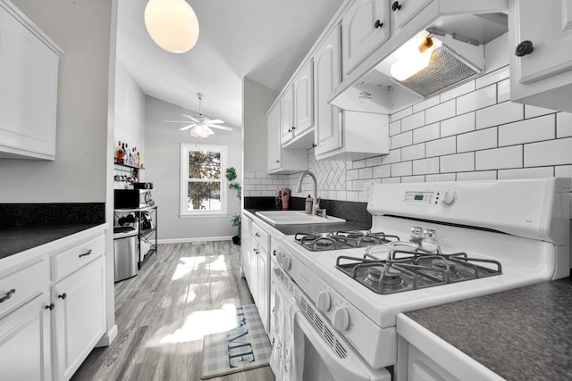 kitchen featuring vaulted ceiling, extractor fan, white cabinetry, white gas range, and sink