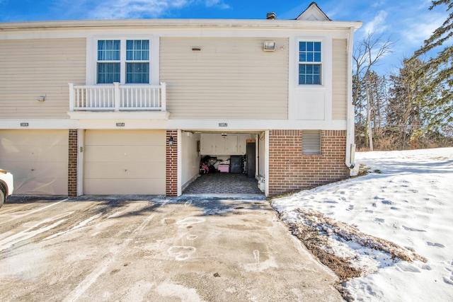 snow covered house featuring a garage and a balcony