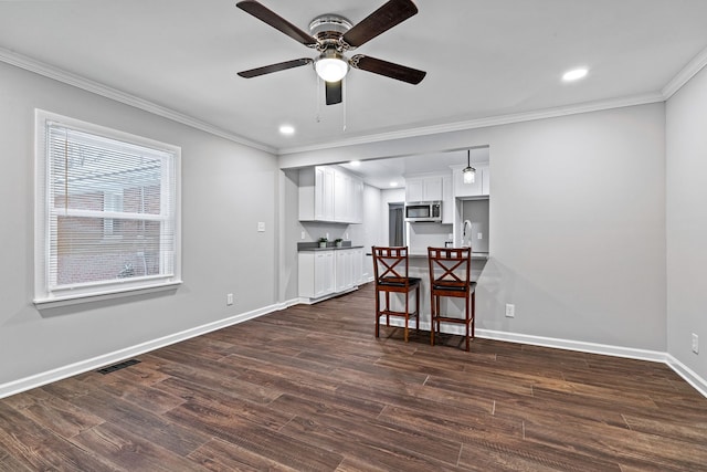 interior space featuring dark hardwood / wood-style floors, white cabinetry, a breakfast bar area, ceiling fan, and crown molding