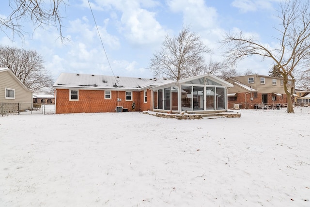 snow covered rear of property featuring a sunroom