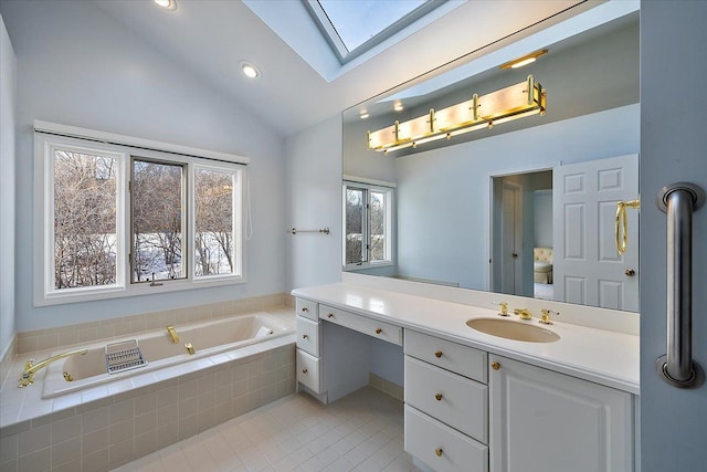 bathroom with tiled tub, lofted ceiling with skylight, vanity, and tile patterned floors