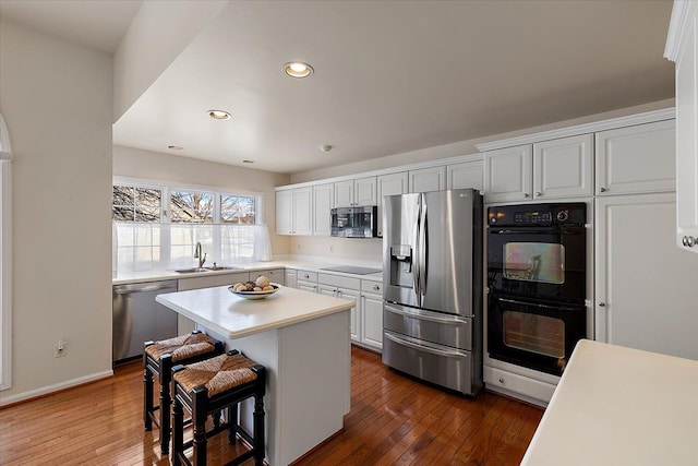 kitchen featuring a breakfast bar, sink, white cabinets, a center island, and black appliances