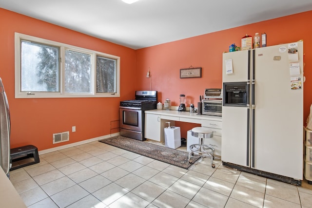 kitchen featuring light tile patterned flooring, white refrigerator with ice dispenser, and gas stove