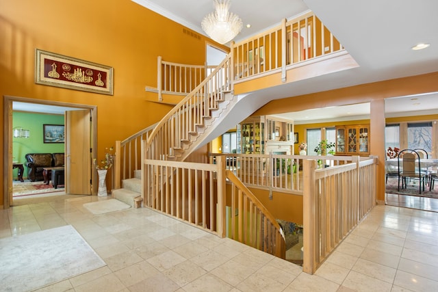 staircase with tile patterned flooring, crown molding, a towering ceiling, and a notable chandelier