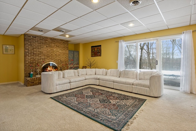 living room with a brick fireplace, carpet floors, and a drop ceiling