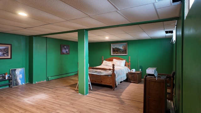 bedroom with wood-type flooring, a baseboard heating unit, and a drop ceiling