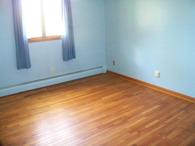 unfurnished room with baseboards, baseboard heating, and wood finished floors