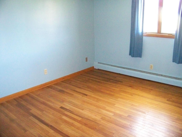 spare room featuring a baseboard heating unit, baseboards, and wood finished floors