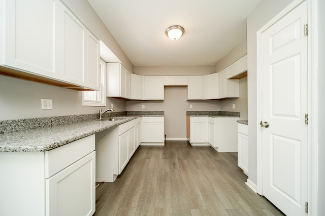 kitchen featuring sink, light stone countertops, light hardwood / wood-style floors, and white cabinets