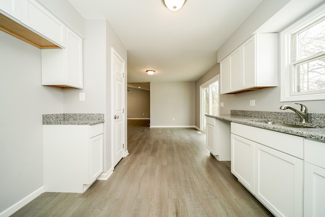 kitchen featuring light hardwood / wood-style floors, light stone countertops, sink, and white cabinets