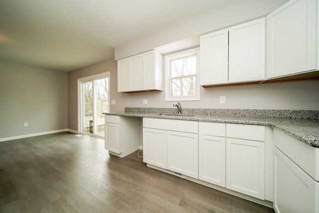 kitchen with white cabinetry, sink, light stone counters, and hardwood / wood-style flooring