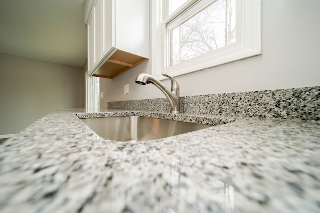 room details featuring light stone counters, sink, and white cabinets