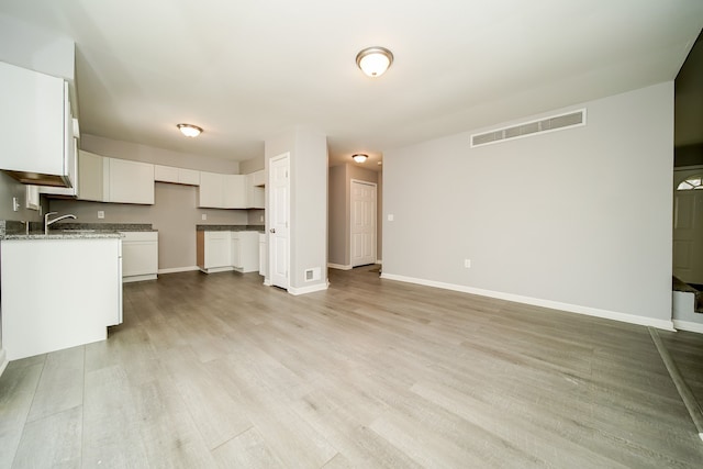 kitchen with white cabinetry, light stone counters, and light hardwood / wood-style flooring