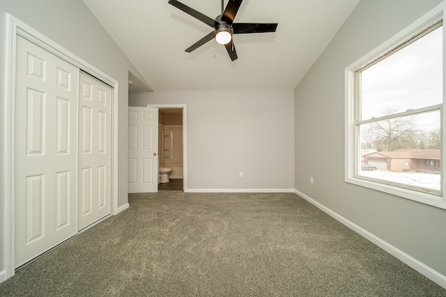 unfurnished bedroom featuring ceiling fan, ensuite bathroom, dark carpet, vaulted ceiling, and a closet