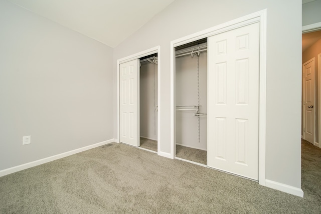 unfurnished bedroom featuring multiple closets, lofted ceiling, and carpet flooring