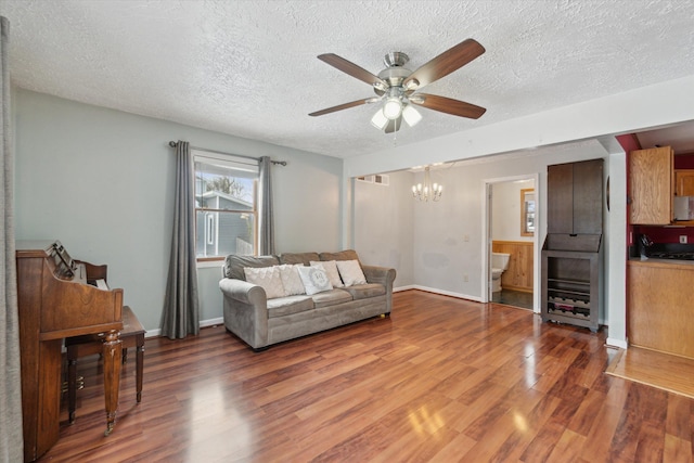 living room featuring hardwood / wood-style flooring, ceiling fan with notable chandelier, and a textured ceiling