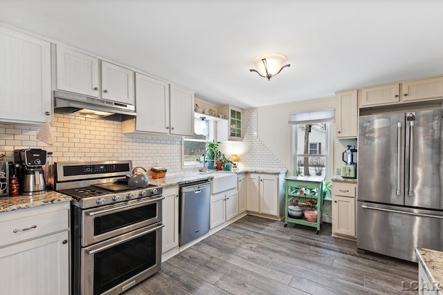 kitchen featuring stainless steel appliances, tasteful backsplash, light stone countertops, and dark wood-type flooring