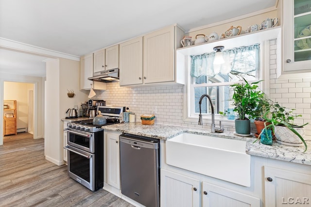 kitchen with appliances with stainless steel finishes, sink, decorative backsplash, light stone counters, and light hardwood / wood-style flooring