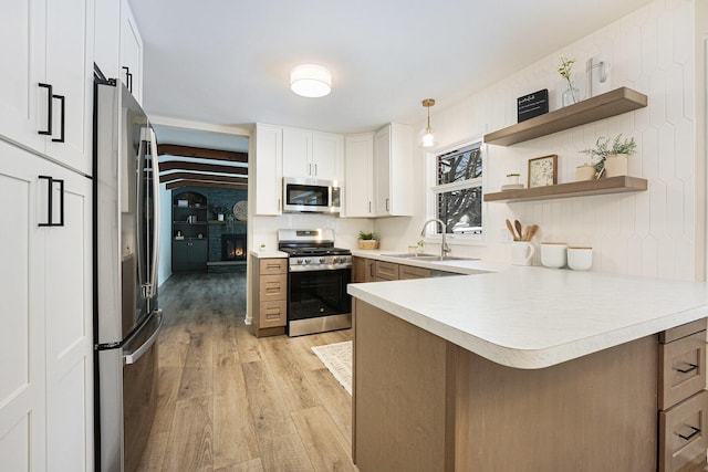 kitchen with sink, stainless steel appliances, white cabinets, decorative light fixtures, and kitchen peninsula