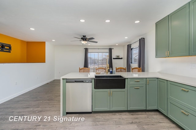 kitchen featuring light wood finished floors, green cabinetry, light countertops, stainless steel dishwasher, and a sink