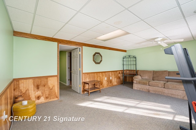 carpeted living room featuring a paneled ceiling, wainscoting, ceiling fan, and wooden walls