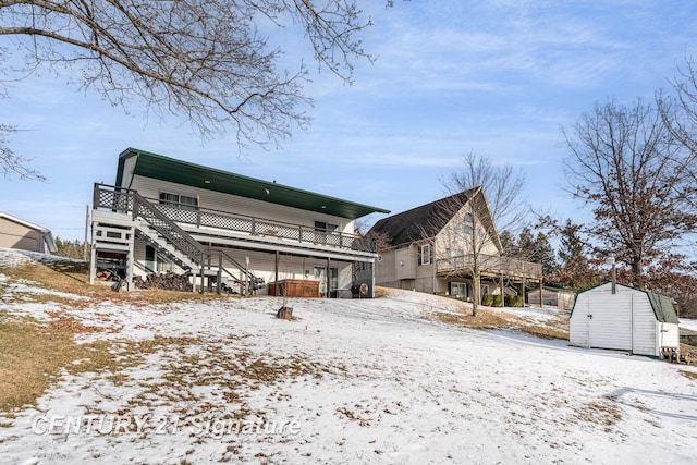 snow covered property with an outbuilding, a storage unit, stairway, and a wooden deck