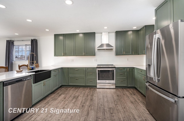 kitchen featuring dark wood-style floors, stainless steel appliances, green cabinets, a sink, and wall chimney exhaust hood