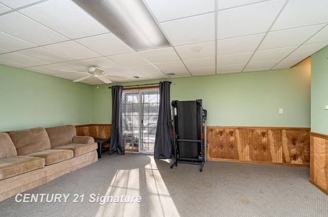 living room featuring carpet floors, a wainscoted wall, wooden walls, and a drop ceiling