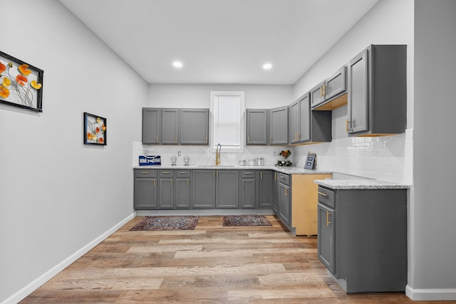 kitchen featuring gray cabinets, tasteful backsplash, sink, light stone counters, and light hardwood / wood-style flooring