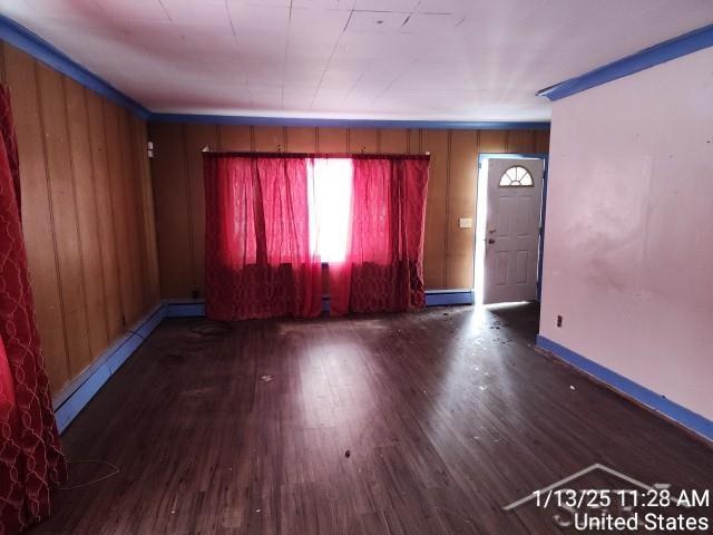 spare room featuring wooden walls, dark hardwood / wood-style flooring, and a baseboard heating unit