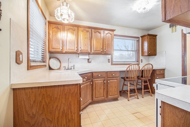 kitchen with brown cabinetry, built in study area, stove, light countertops, and a sink