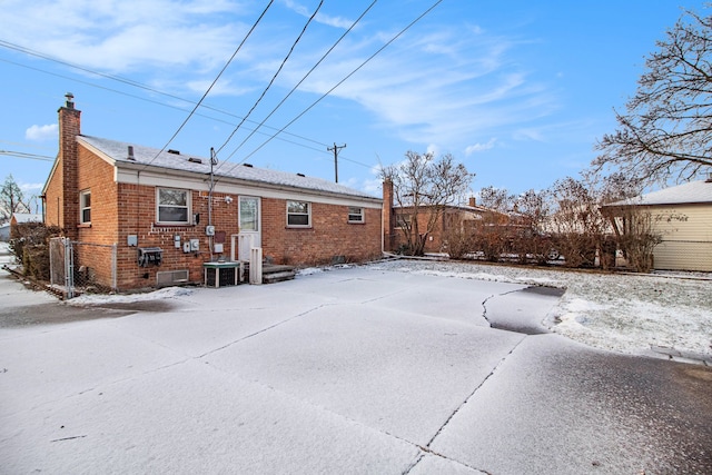 snow covered house with brick siding, fence, a chimney, and central AC unit