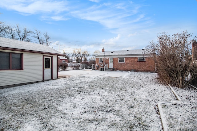 snow covered house featuring brick siding and a chimney