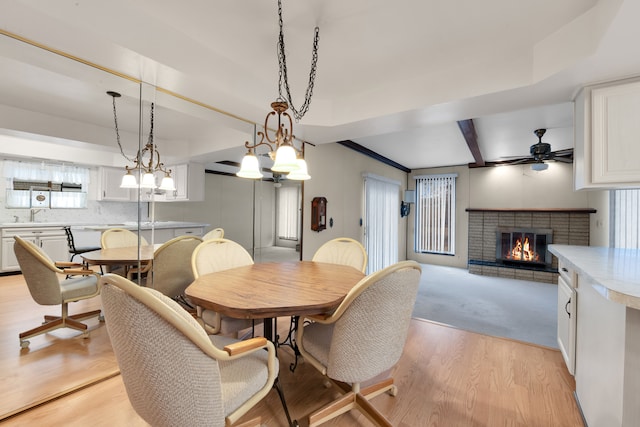 dining space featuring sink, a brick fireplace, light hardwood / wood-style flooring, beamed ceiling, and ceiling fan